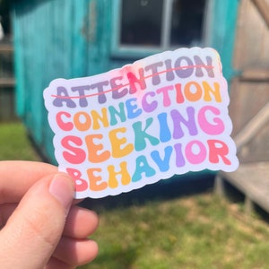 May include: A rainbow sticker with the words "Attention Seeking Behavior" in a colorful, bubbly font.