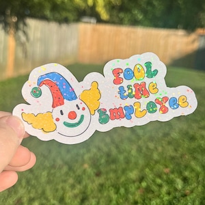 May include: A white sticker with a colorful cartoon clown and the text "Fool time Employee" in rainbow glitter letters.