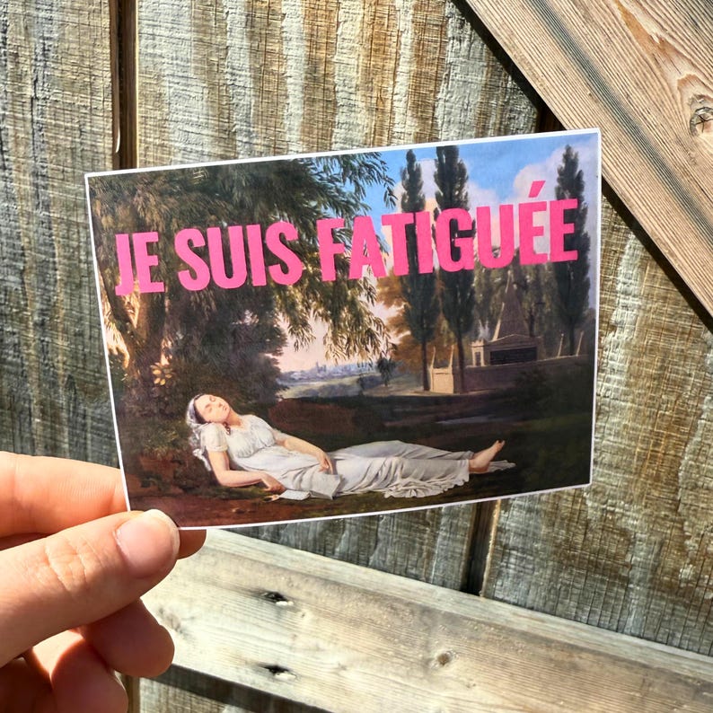 May include: A sticker with a painting of a woman lying down in a field. The text "JE SUIS FATIGU&Eacute;E" is printed in pink on the sticker.