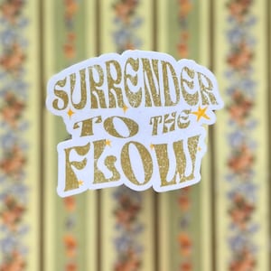 May include: White sticker with gold lettering that reads "Surrender to the Flow" with small gold stars scattered around the text.