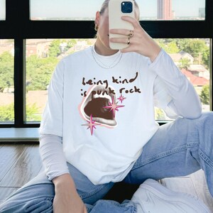Comfort Colors 1717 Shirt
Color: White
Graphic: open screaming mouth in a retro halftone print, surrounded by pink stars and starbursts, with the handwritten phrase “Being Kind is Punk Rock” above in brown lettering