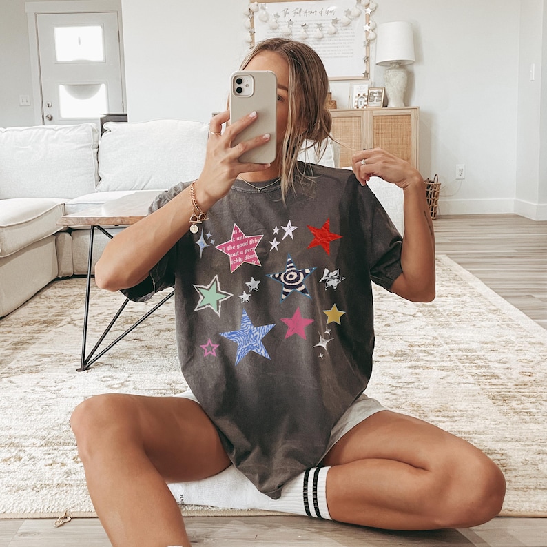 Comfort Colors 1717 T-Shirt
Color: Pepper (textured gray)
Graphic: Colorful collage-style star graphic featuring various hand-drawn and patterned stars scattered across the chest. The stars include a mix of animal prints, stripes, solid colors, and textures, with some metallic and doodle-like accents.
keywords: early 2000s, y2k streetwear, cool girl aesthetic, baddie, whimsigoth, whimsical, whimsy goth tops, soft grunge, summer outfit, music festival, rave, alt clothing, trending tops women