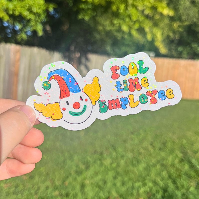 May include: A white sticker with a colorful cartoon clown face and the text "FOOL time EMPLOYEE" in rainbow letters. The sticker has a glittery finish.