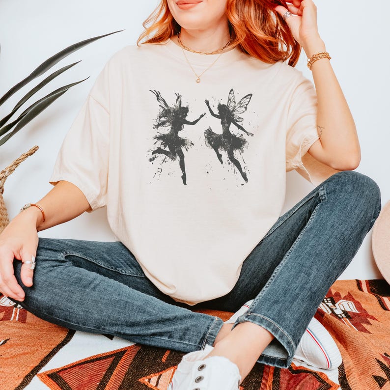 Tshirt Color: Ivory/ Off white
Image: Black Silhouette image of two dancing and frolicking fairies with grunge texture

Keyword: Dark Academia, Goblincore, Fairycore, Oversized boho, Forestcore, Dancing Faeries, Forest