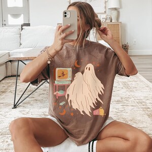 Comfort Colors 1717 Shirt
Color: Espresso (Brown)
Graphic: Two cartoon-style ghosts watch a witch flying on a TV screen surrounded by stars, popcorn, VHS tapes, and crescent moons.
Keywords: keywords: whimsical, mystical, ghost tshirt, vintage halloween, 90s halloween party, scary movies, whimsigoth, whimsygoth, gothic, retro 70s, witchy gift idea, witchcore, salem witch, alt clothing, alternative womens fashion, cozy fall, comfy, haunted house, halloween party, autumn