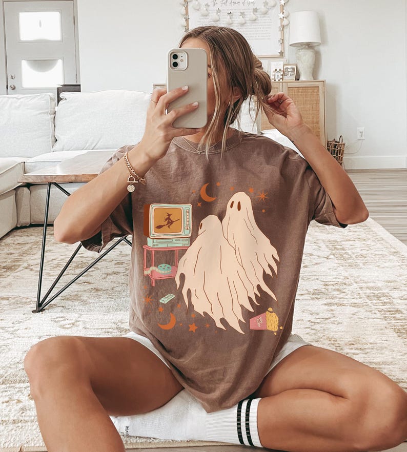 Comfort Colors 1717 Shirt
Color: Espresso (Brown)
Graphic: Two cartoon-style ghosts watch a witch flying on a TV screen surrounded by stars, popcorn, VHS tapes, and crescent moons.
Keywords: keywords: whimsical, mystical, ghost tshirt, vintage halloween, 90s halloween party, scary movies, whimsigoth, whimsygoth, gothic, retro 70s, witchy gift idea, witchcore, salem witch, alt clothing, alternative womens fashion, cozy fall, comfy, haunted house, halloween party, autumn