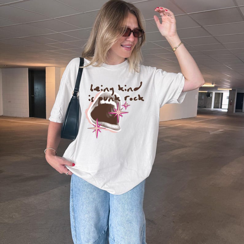 Comfort Colors 1717 Shirt
Color: White
Graphic: open screaming mouth in a retro halftone print, surrounded by pink stars and starbursts, with the handwritten phrase “Being Kind is Punk Rock” above in brown lettering