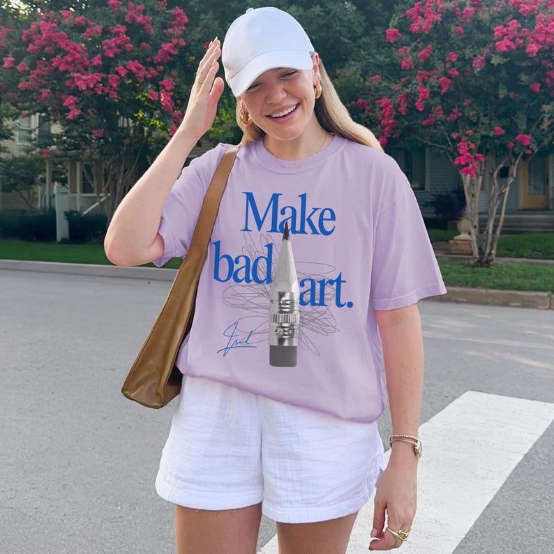Comfort Colors 1717 Shirt
Color: Orchid (light purple)
Graphic: Bold blue text that reads ‘Make bad art' behind a pencil graphic, with scribble doodle lines in gray and a signature-style accent in bottom corner
