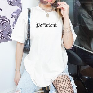 May include: A white oversized t-shirt with the word "Deficient" printed in black gothic font.