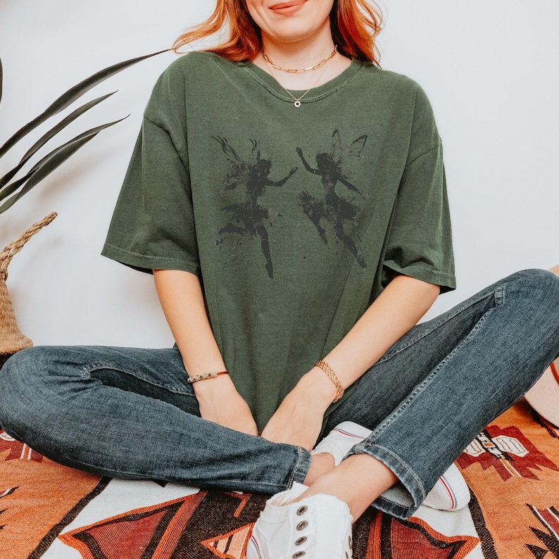 Tshirt Color: Moss / Dark Green
Image:Black Silhouette image of two dancing and frolicking fairies with grunge texture

Keywords: Fairy Grunge Shirt, Fairycore TShirt, Whimsigoth Clothing, Dancing Fairies