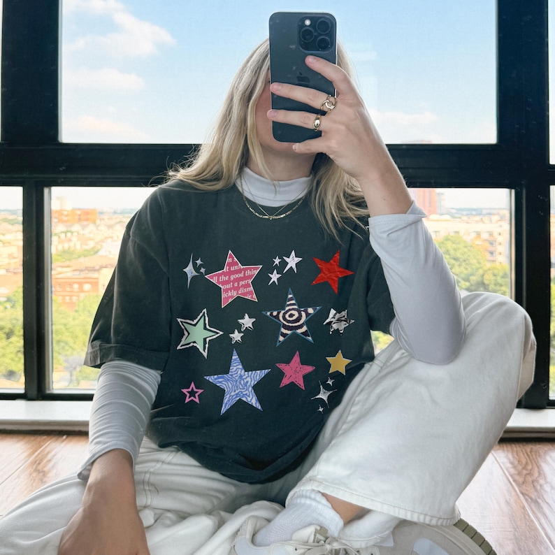 Comfort Colors 1717 T-Shirt
Color: Pepper (textured gray)
Graphic: Colorful collage-style star graphic featuring various hand-drawn and patterned stars scattered across the chest. The stars include a mix of animal prints, stripes, solid colors, and textures, with some metallic and doodle-like accents.