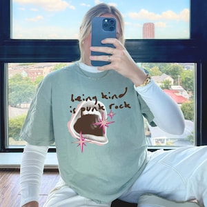 Comfort Colors 1717 Shirt
Color: Bay (light green blue)
Graphic: open screaming mouth in a retro halftone print, surrounded by pink stars and starbursts, with the handwritten phrase “Being Kind is Punk Rock” above in brown lettering