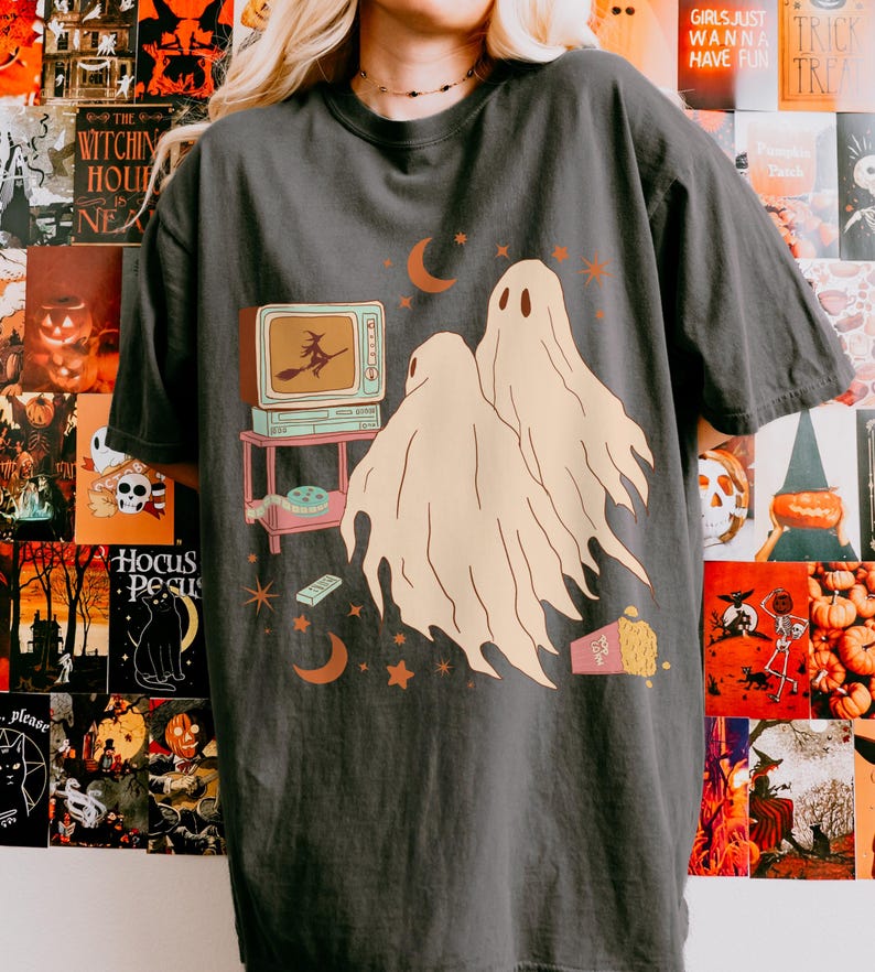 Comfort Colors 1717 Shirt
Color: Pepper (textured gray)
Graphic: Two cartoon-style ghosts watch a witch flying on a TV screen surrounded by stars, popcorn, VHS tapes, and crescent moons.