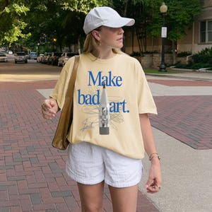 Comfort Colors 1717 Shirt
Color: Butter Yellow
Graphic: Bold blue text that reads ‘Make bad art' behind a pencil graphic, with scribble doodle lines in gray and a signature-style accent in bottom corner