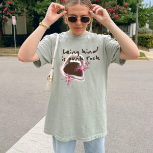 Comfort Colors 1717 Shirt
Color: Bay (light green blue)
Graphic: open screaming mouth in a retro halftone print, surrounded by pink stars and starbursts, with the handwritten phrase “Being Kind is Punk Rock” above in brown lettering