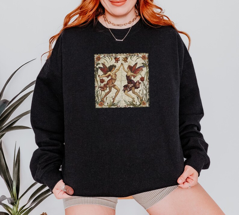 May include: Black sweatshirt with a vintage illustration of two fairies dancing in a floral frame.