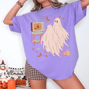 Comfort Colors 1717 Shirt
Color: Violet (purple)
Graphic: Two cartoon-style ghosts watch a witch flying on a TV screen surrounded by stars, popcorn, VHS tapes, and crescent moons.
keywords: pumpkin patch outfit, celestial, cute ghosts, oversized y2k, pastel goth, soft grunge, gift for girlfriend