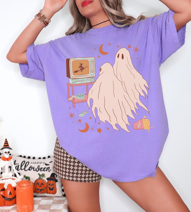 Comfort Colors 1717 Shirt
Color: Violet (purple)
Graphic: Two cartoon-style ghosts watch a witch flying on a TV screen surrounded by stars, popcorn, VHS tapes, and crescent moons.
keywords: pumpkin patch outfit, celestial, cute ghosts, oversized y2k, pastel goth, soft grunge, gift for girlfriend
