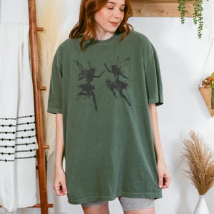 May include: A green oversized t-shirt with a graphic print of two fairies in silhouette.