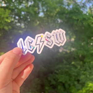 May include: A white sticker with the text "LCSW" in a bold, 3D-style font. A lightning bolt is in between the "L" and "C". The sticker has a holographic finish that shimmers in different colors.