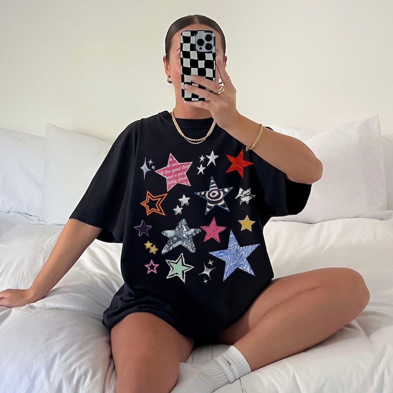 Comfort Colors 1717 T- Shirt
Color: Black
Graphic: bold star graphic design in multiple colors and textures. Features a mix of embroidered, metallic, and printed stars, along with abstract celestial details.

Keywords: Music Festival Rave Outfit, Casual, Comfy, Leopard Star, Pinterest Style, Retro 90s, Abstract, Cosmic-inspired, Art Hoe, Artist Gift, Colorful, Texture, Casual street style, Indie