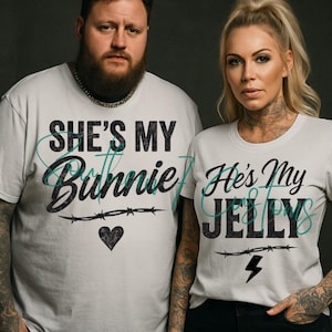 Puede incluir: Dos personas con camisetas blancas a juego. Una camiseta dice "She's My Bunnie" con un corazón y un diseño de alambre de púas. La otra camiseta dice "He's My Jelly" con un rayo y un diseño de alambre de púas. Las camisetas son de manga corta.