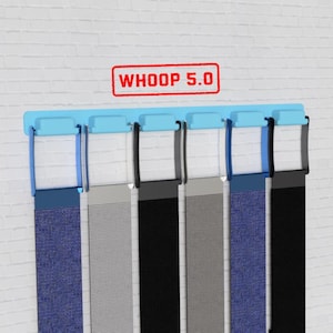Op de afbeelding: Een displayrek met zes fitnessbanden in verschillende kleuren, waaronder blauw, grijs en zwart. De banden hangen aan een lichtblauwe houder. De tekst "WHOOP 5.0" wordt boven het rek weergegeven in een rode rechthoek.