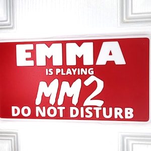 May include: Red sign with white text that reads "Emma is playing MM2 Do Not Disturb".