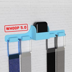 May include: A light blue wall-mounted holder with a black device and several watch bands. The holder has the text "WHOOP 5.0" in a red box. The watch bands are in various colors, including blue, silver, black, and gray.