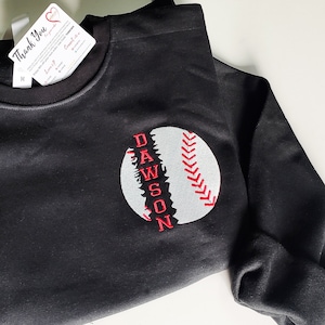 May include: Black sweatshirt with a white baseball graphic and the name "DAWSON" embroidered in red on the front.