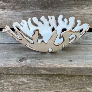 May include: White ceramic bowl with a unique organic shape and brown glaze accents. The bowl is designed with a series of irregular, flowing curves and edges, resembling a natural form like coral or a leaf.