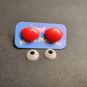 May include: Two red plastic eyes with a white backing, and two white plastic eyes with black pupils. The eyes are on a blue card with the text "Meow Magic".