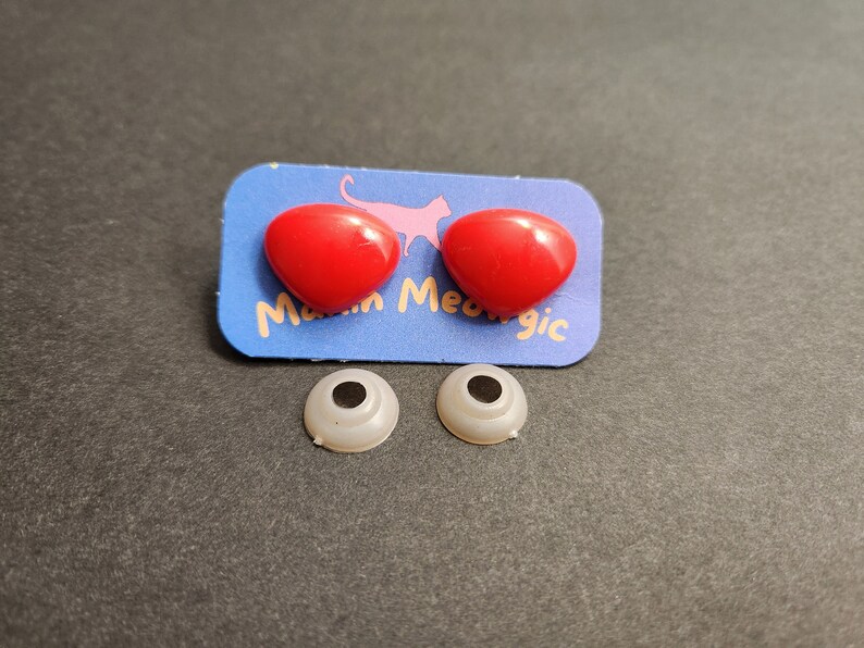 May include: Two red plastic eyes with a white backing, and two white plastic eyes with black pupils. The eyes are on a blue card with the text "Meow Magic".
