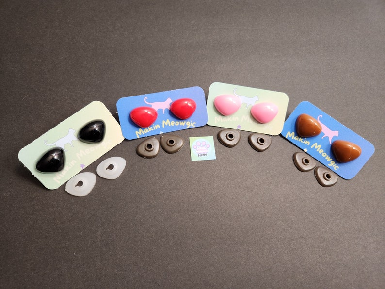 May include: Four pairs of plastic safety eyes for crafts, in black, red, pink, and brown. Each pair is packaged on a card with a cat illustration and the text "Makin Meowgic".