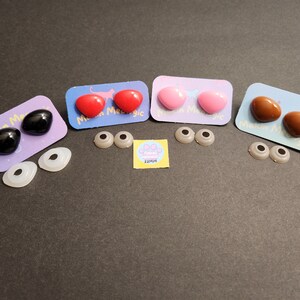 May include: Four pairs of plastic safety eyes for crafts, in black, red, pink, and brown. Each pair is packaged on a card with the text "Mini Magic" and a paw print with the text "22MM".