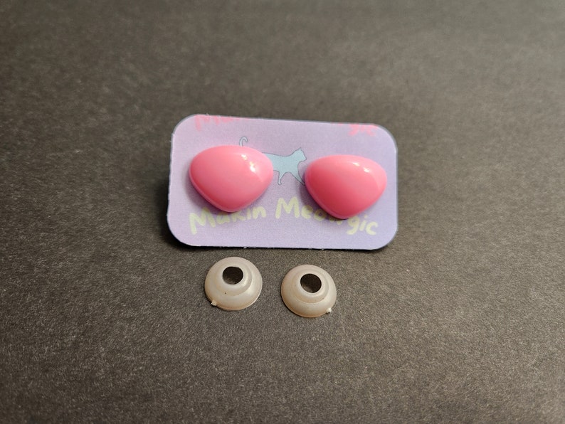 May include: Two pink plastic safety eyes and two white plastic safety eye sockets. The safety eyes are on a purple card with the text "Make Me Magic".