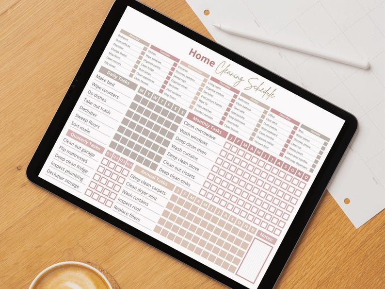 May include: A printable cleaning schedule on a tablet with a brown wooden background. The schedule is divided into daily, weekly, monthly, and annual tasks. Each task has a checkbox next to it. The schedule is designed to help people stay organized and on top of their cleaning.