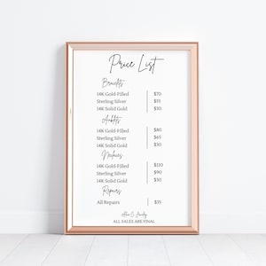 Op de afbeelding: Een ingelijste prijslijst voor sieraden, met categorie&euml;n zoals armbanden, enkelbanden, kettingen en reparaties. De lijst bevat prijzen voor 14K goudgevulde, sterling zilveren en 14K massief gouden items. De lijst heeft een ros&eacute;gouden frame.