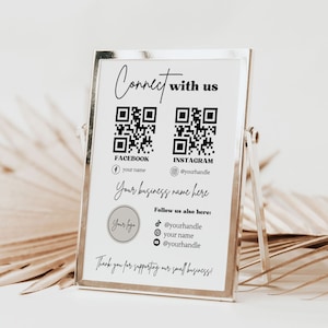 Könnte beinhalten: Ein weißes Schild in einem silbernen Rahmen mit einem schwarz-weißen QR-Code für Facebook und Instagram. Das Schild sagt "Connect with us" und enthält Social-Media-Handles für Facebook und Instagram. Das Schild sagt auch "Your business name here" und "Thank you for supporting our small business!"
