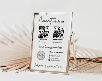 May include: A white sign in a silver frame with a black and white QR code for Facebook and Instagram. The sign says "Connect with us" and includes social media handles for Facebook and Instagram. The sign also says "Your business name here" and "Thank you for supporting our small business!"