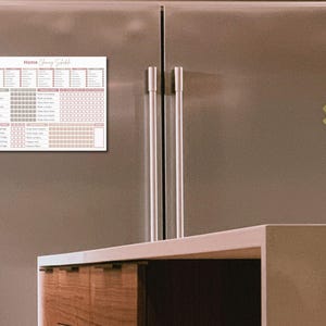 May include: A white magnetic cleaning schedule chart with the text "Home Cleaning Schedule" in pink script. The chart is attached to a stainless steel refrigerator.