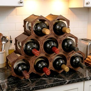 May include: A dark brown wooden wine rack with a modular honeycomb structure. The rack features hexagonal compartments, each holding a glass wine bottle with a dark liquid. The wood panels are decorated with small, etched grape vine illustrations.