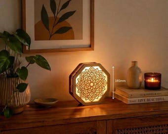 May include: An octagonal wooden lamp featuring an intricate laser-cut mandala pattern that emits a warm glow. The lamp stands 165mm tall, as indicated by a vertical measurement arrow, and is placed on a wooden surface next to books and a candle.