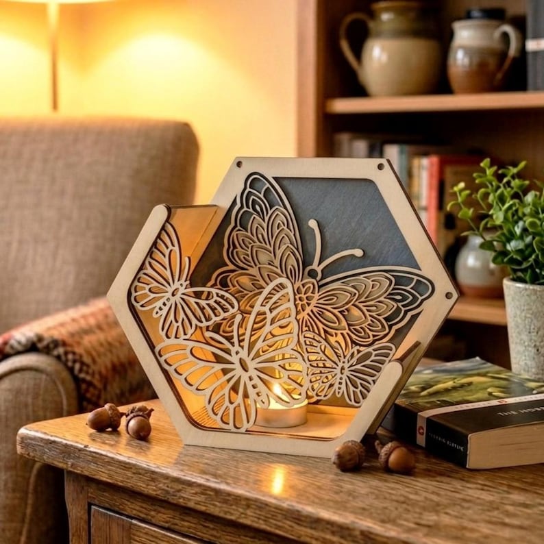 May include: A wooden, hexagonal candle holder with a butterfly design. The intricate design features laser-cut butterflies, with a small candle inside. The holder is made of light-colored wood and sits on a wooden table.