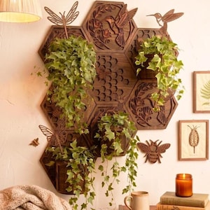 May include: A wooden wall planter with a honeycomb design, featuring hexagon-shaped shelves holding potted plants with trailing green vines. Decorative laser-cut hummingbirds, butterflies, and bees adorn the dark brown wood, creating a nature-inspired display.