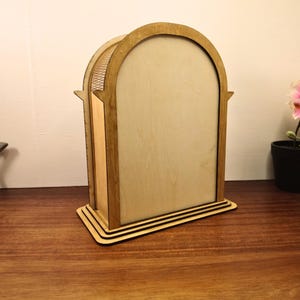 May include: A wooden arched display case with a light brown finish. The case has a rectangular base with three layered tiers. The arched top has a decorative, openwork design. The interior is a lighter shade of wood.