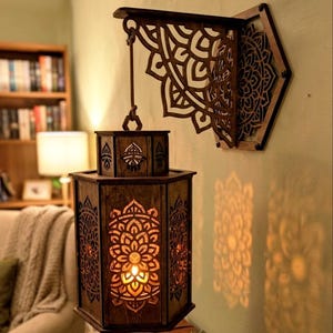 May include: A dark brown wooden wall-mounted lantern featuring intricate laser-cut mandala patterns on its hexagonal panels. The lantern hangs from a decorative, matching wooden bracket attached to the wall, casting warm light through the cutouts.