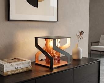 May include: A modern wooden table lamp with a black frame and a warm, glowing light. The lamp features a unique design with layered wooden elements and sits on a dark wooden surface. Books are stacked nearby.