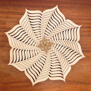 May include: A wooden, laser-cut decorative piece in the shape of a flower. The design features layered, curved lines radiating outwards from a central floral motif. The natural wood tones create a warm, inviting aesthetic. The piece is displayed on a wooden surface.