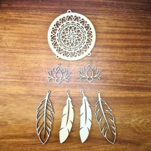 May include: A selection of laser-cut wooden craft shapes, including a circular mandala, two lotus flower shapes, and four feather shapes. The items are light-coloured and arranged on a wooden surface, suitable for jewellery making or other crafts.